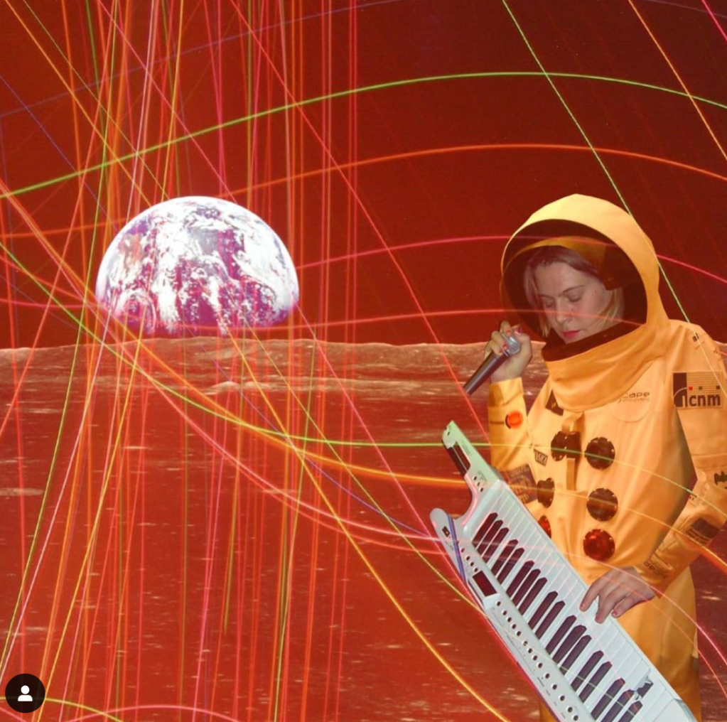 The artist Anna Oxygen playing a keytar in an orange space hooding with a projection of the moon behind them and a grid of light.