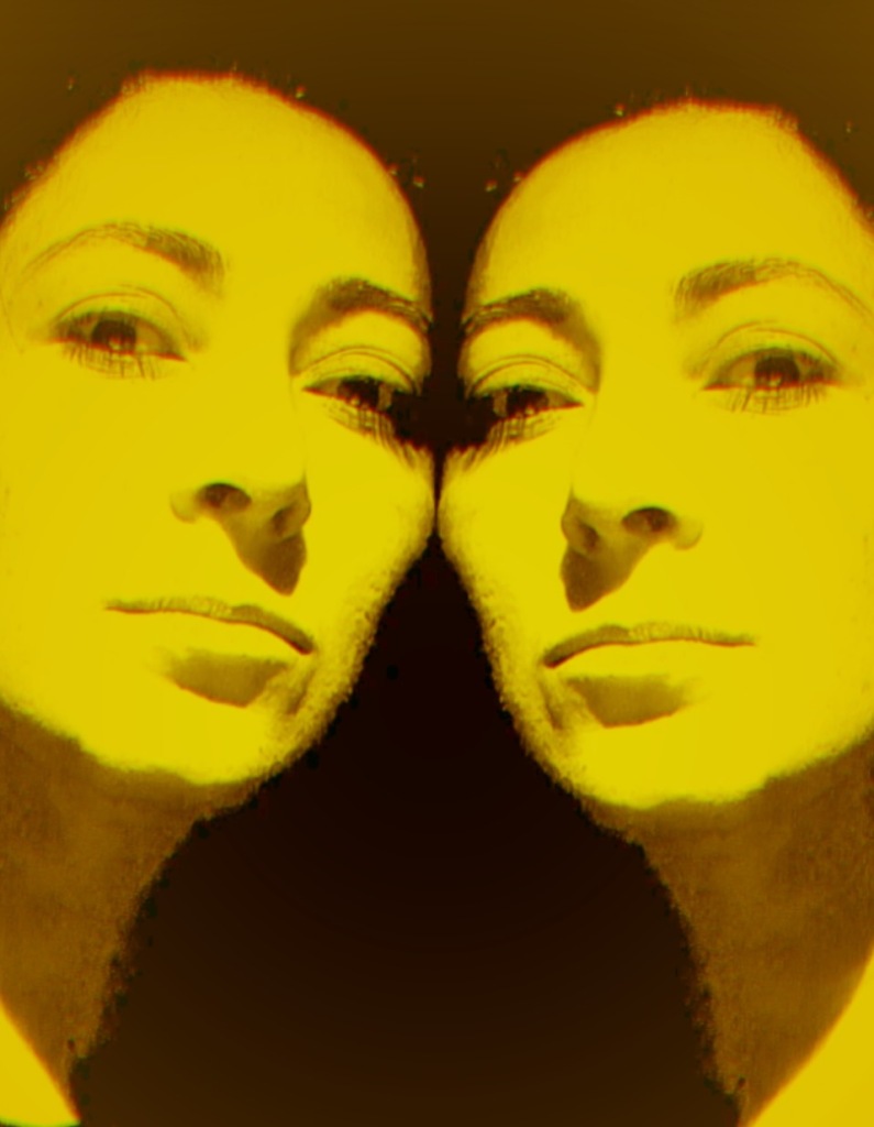 A double image of Karyna Herrera in a yellow and brown hue, where the artists upper cheekbones meet. There gaze holds us, their mouths in defiant line.